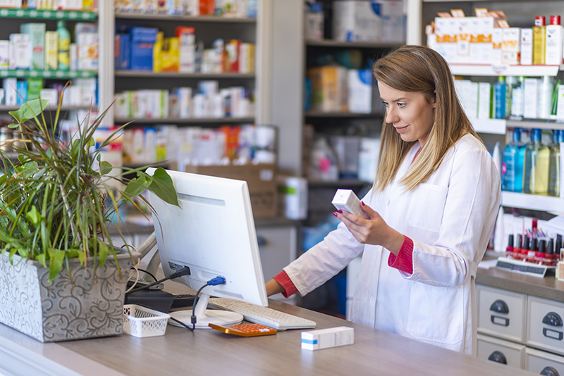 FemalePharmacistHoldingPrescriptionandUsingComputerinPharmacy